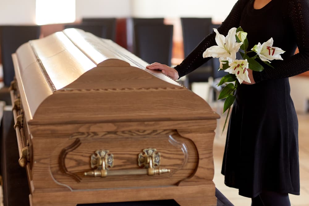 Woman holding white lily flowers beside coffin at funeral service in church, representing mourning concept.