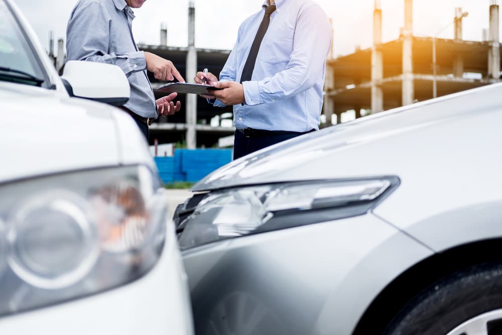 Insurance agent carefully inspecting and documenting a car after an accident, diligently noting details on a clipboard during the claim assessment and processing.