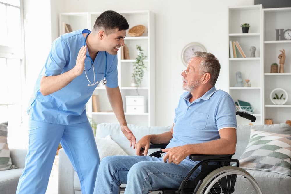 Vulnerable senior man in wheelchair feeling frightened in the presence of an upset caregiver at home.