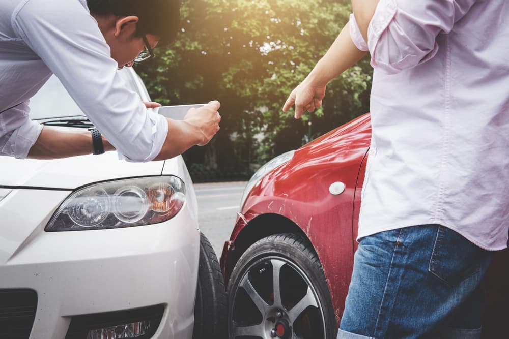 Two drivers arguing after a car accident, one making a phone call to an insurance agent. Traffic accident and insurance concept.