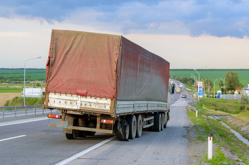 Semi-truck with burst tires on highway street, indicating a flat-out and damaged situation.