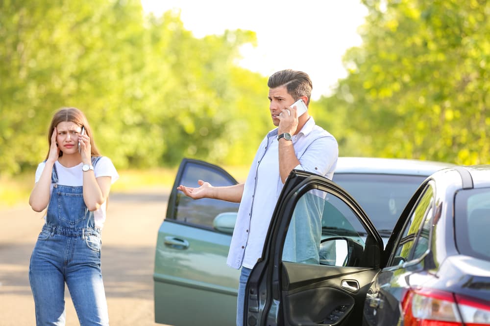 Anxious drivers standing beside damaged vehicles following a car accident.