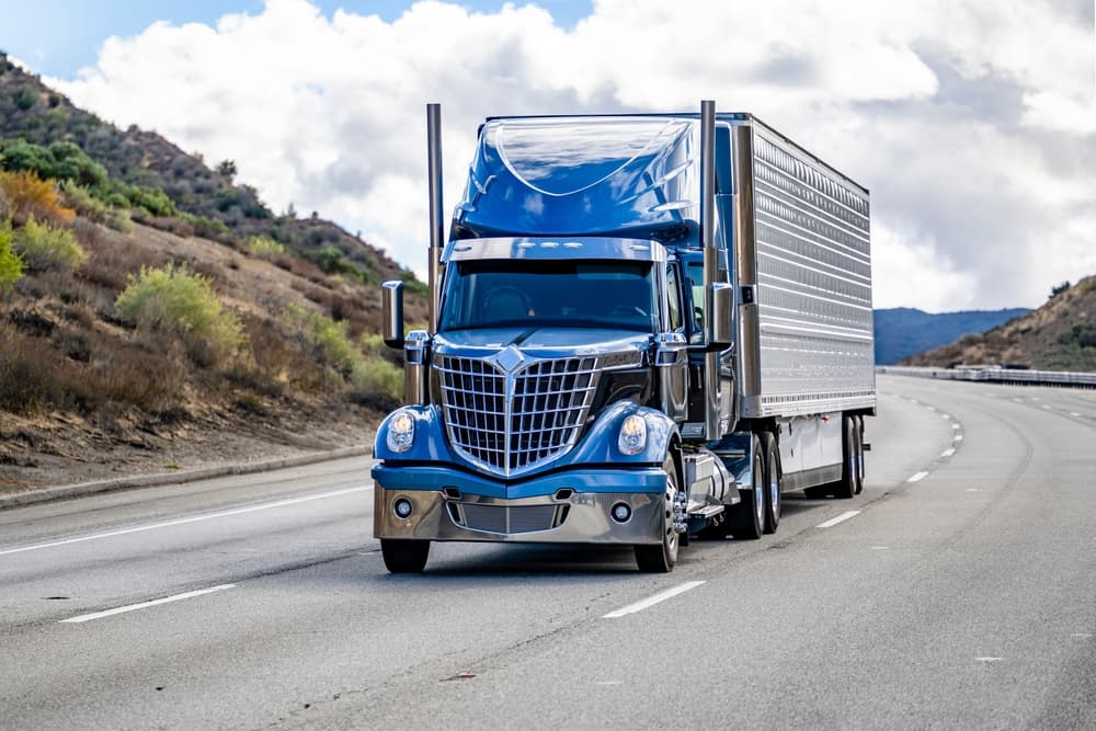 Blue semi-truck hauling frozen cargo in refrigerated trailer on highway.