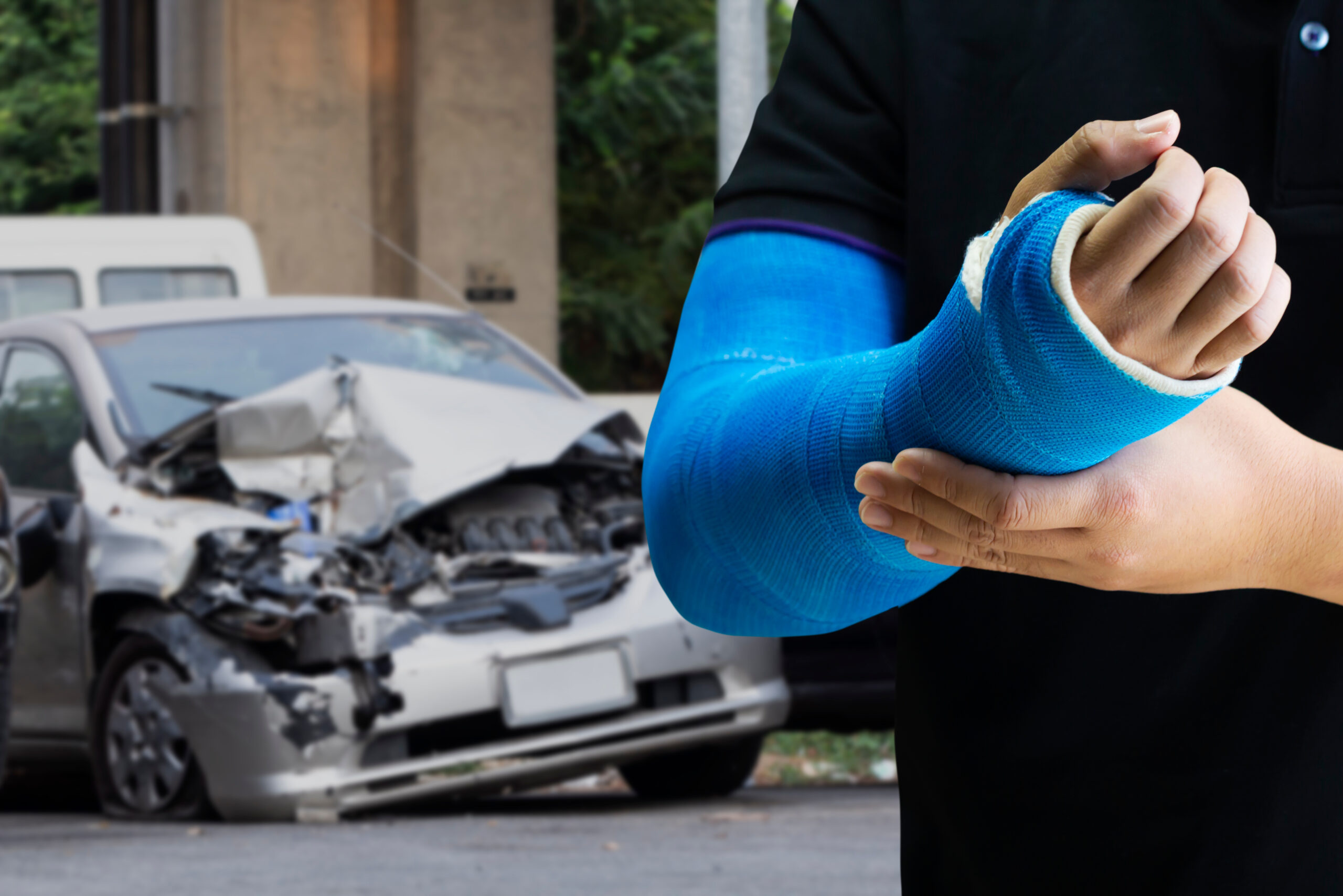Person with a blue cast on their arm in front of a blurred car accident scene