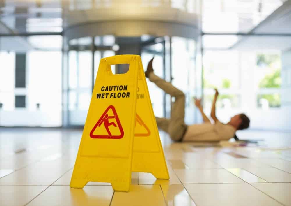Wet floor caution sign in hallway as man slips and falls in workplace accident.