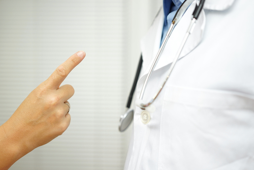 A person points a finger accusingly at a doctor wearing a white coat and stethoscope, suggesting a confrontation or medical dispute.