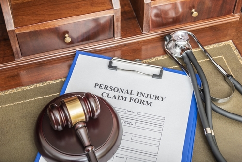 A clipboard with a personal injury claim form, placed on a wooden desk beside a gavel and a stethoscope, symbolises a legal and medical assessment.