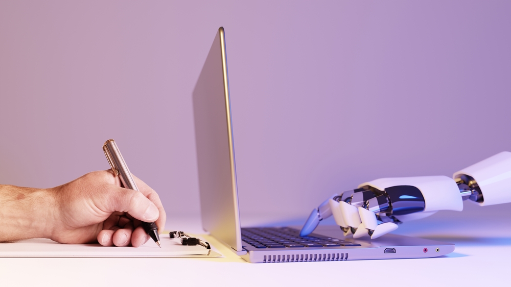 Human hand writing with a pen beside a robotic hand typing on a laptop keyboard, symbolizing collaboration between AI and humans.