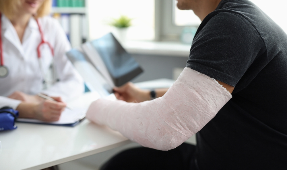 A man with a broken arm in a pink cast discusses his X-ray results with a doctor during a medical consultation.