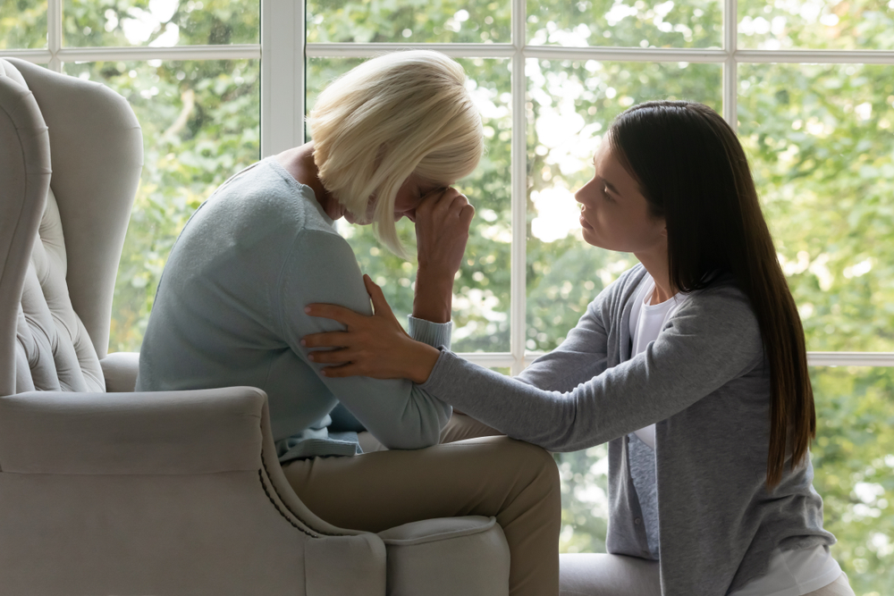 Young woman comforting an older woman sitting by a window, representing grief, loss, and the emotional impact of wrongful death