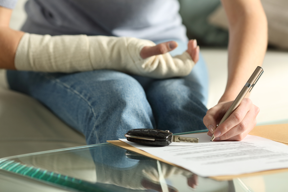 A person with a bandaged arm signing documents next to car keys.