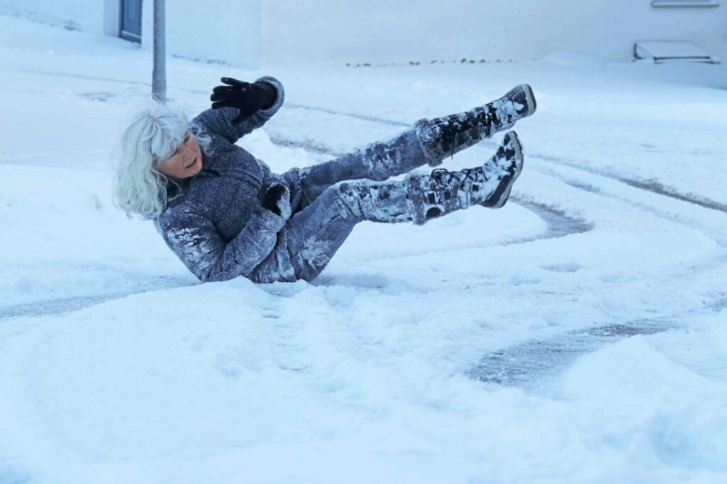 Mujer mayor resbalando y cayendo en una acera con hielo durante condiciones invernales de nieve. Mujer mayor resbalando y cayendo en una acera con hielo durante condiciones invernales de nieve.